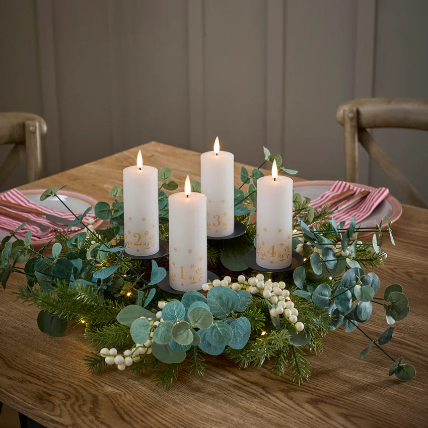 Adventsdeko mit vier LED-Adventskerzen, Eukalyptus und Tannengrün auf einem Holztisch