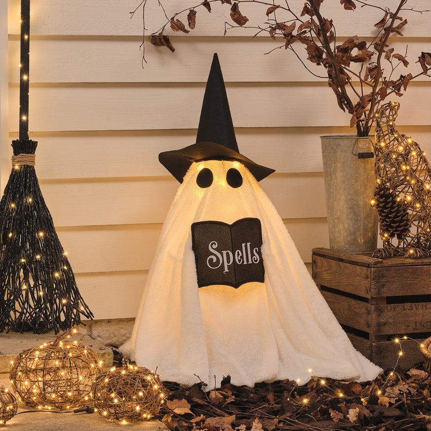 Halloween-Deko mit leuchtenden Kürbissen, Geist, Katze, Hexenbesen und Kerzen vor einer Haustür.