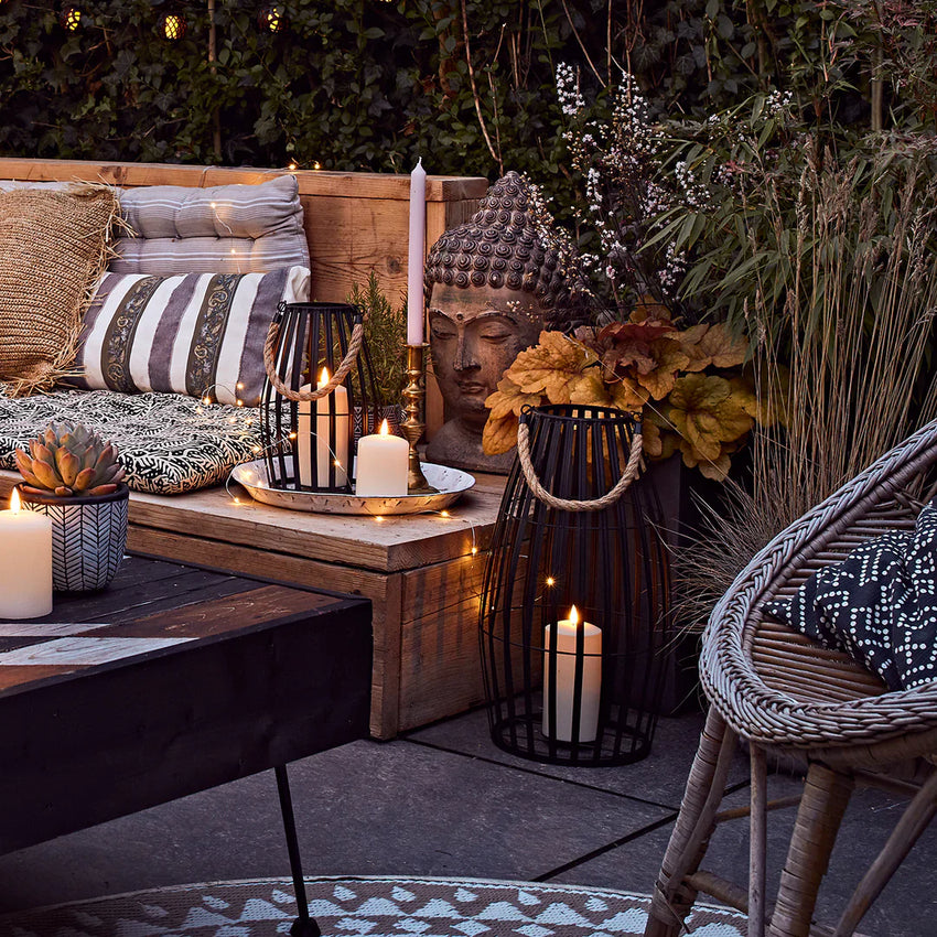 Sommerlich dekorierte Outdoor-Lounge mit Kerzen, Laternen, Kissen und warmen Lichtern.