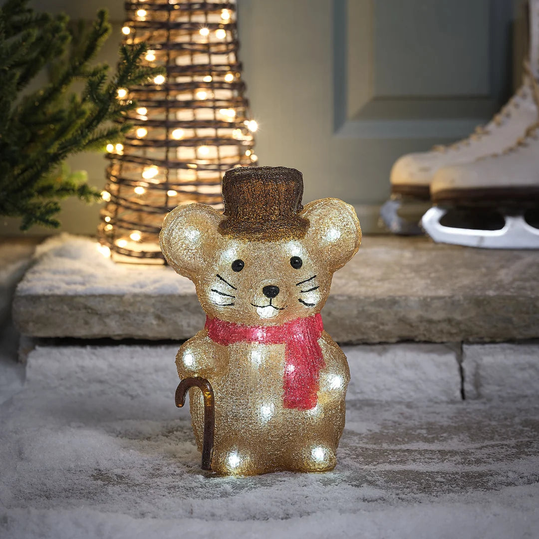 Charmante glitzernde goldene Maus-Dekofigur mit roter Weihnachtsschleife, positioniert vor beleuchteter Kegel-Weihnachtsbaumdekoration auf Stein-Terrasse – festliche Plüschfigur für Außendekoration, Garten-Arrangements und weihnachtliche Hausdekorationen mit eleganter Glitter-Textur und warmweißer LED-Beleuchtung im Hintergrund.