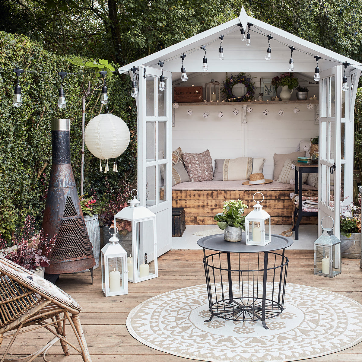 Gartenhaus in Weiß auf Terrasse mit Holzboden und sommerlicher Deko inkl. Deko Laternen.